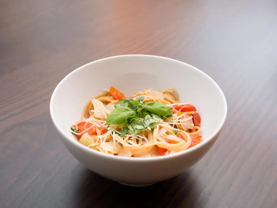 A bowl of pasta with tomatoes, fresh basil and cheese on a wooden table